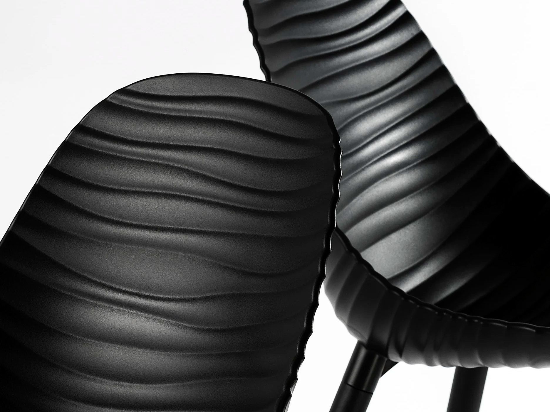 Close detail of two sculptural black chairs with a rippled, wave-like moulded surface.