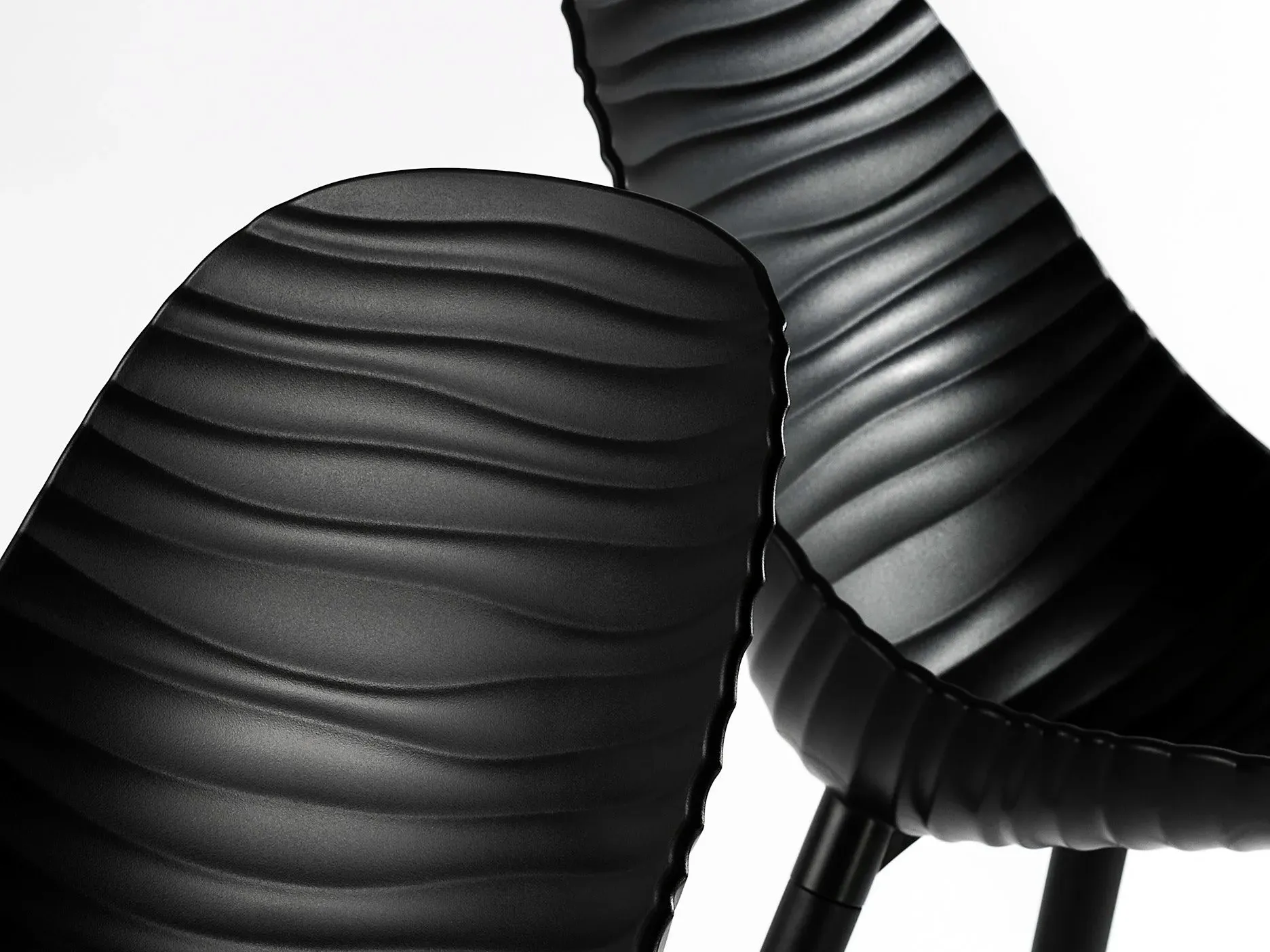 Close detail of two sculptural black chairs with a rippled, wave-like moulded surface.