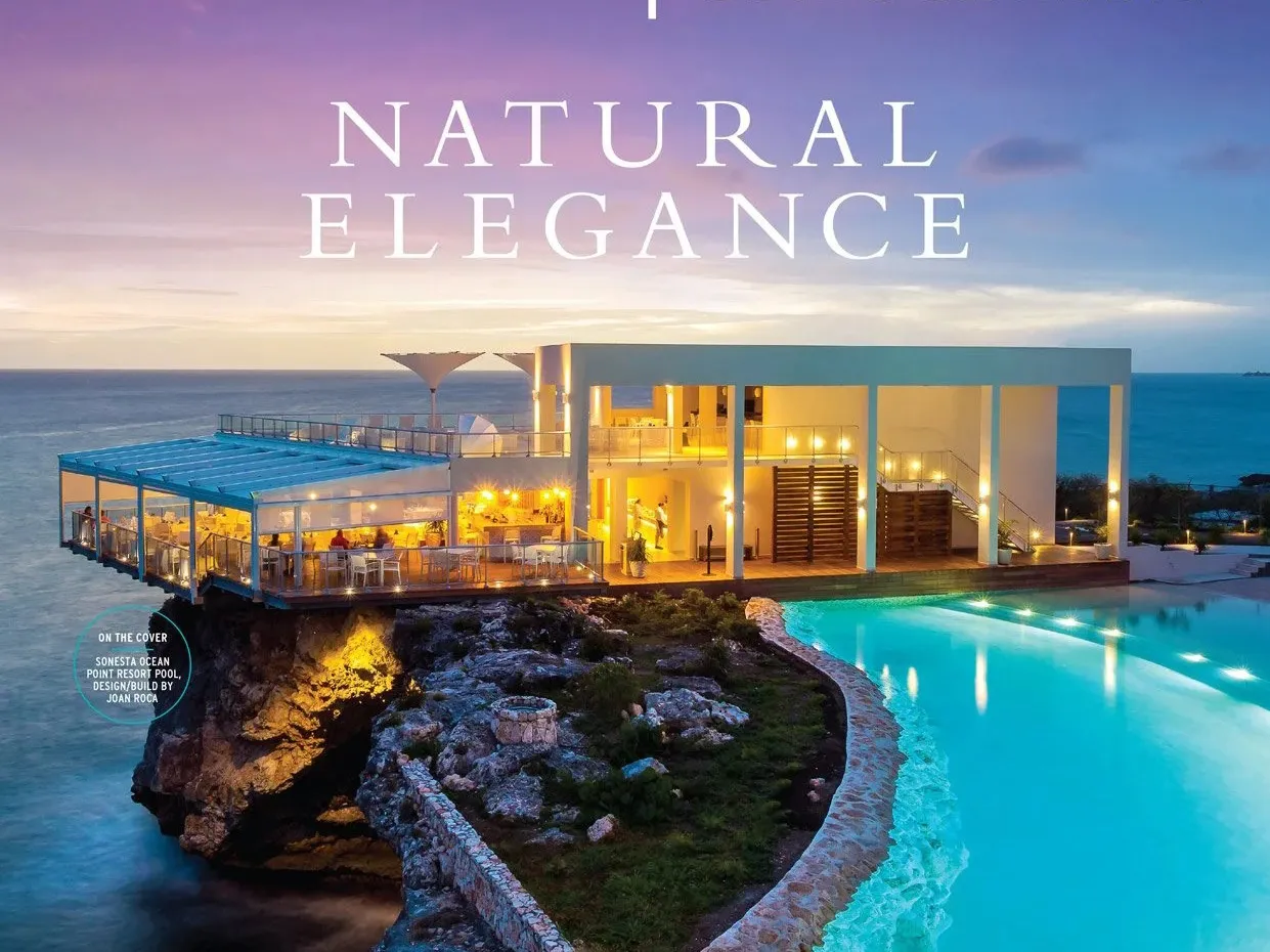Clifftop resort at twilight — a lit restaurant pavilion above an infinity pool over the sea.